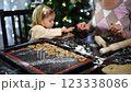 Mom watches as a little girl puts cookie cutters on the dough 123338086