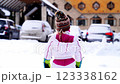 Little girl in a ski suit stands in the snow and looks at the parking lot at the hotel 123338162