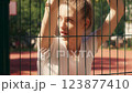 Serious young woman standing behind bars, looking around prison sports court 123877410