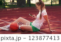 Sportive young woman sitting on sports court, scrolling smartphone, fitness blog 123877413