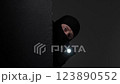 A masked intruder wearing a black balaclava peeks around a corner in the dark, holding a flashlight, evoking mystery. 123890552
