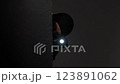 A man wearing a mask and holding a flashlight cautiously examines the surroundings, blending into the dark shadows. 123891062