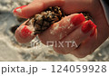 A woman with elegant red manicure holds and turns pine cones in the snow highlighting natural textures and cozy winter vibes with vibrant contrast of snowy background and bold nail color. 124059928