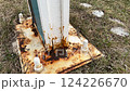 Metal pillar fastened to basement with anchor bolts and nuts. The rusty surface of the post and the fastenings are in places. The support of the iron pillar on a green lawn in the park. Close-up 124226670