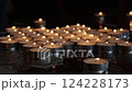 Close-up of burning tealight candles arranged on reflective surface in dark setting. Candlelight and remembrance concept for design and print 124228173