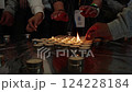 Close-up of hands lighting memorial candles with matches. Group ceremony with tea light candles arranged on a reflective surface. Remembrance and tribute ritual. Jewish cultural and religious 124228184