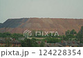 Large industrial waste heap or slag heap from mining operations near a residential area with trees and brick houses. Environmental impact and industrial landscape concept 124228354