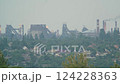 Industrial steel plant with smokestacks and cooling towers emitting smoke and fire behind a residential area with green trees and houses. Environmental pollution and heavy industry concept 124228363