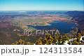 Breathtaking view of a tranquil lake surrounded by lush greenery and distant mountains during a clear sunny day 124313584
