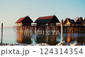 Beautiful waterfront huts reflect on calm water at sunset in a serene lakeside location 124314354