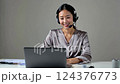 Smiling Woman in Silver Blouse Using Laptop with Headset 124376773