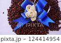 A beautiful arrangement of roasted coffee beans adorned with a vibrant blue ribbon and a delicate cream-colored flower, perfect for coffee lovers and gift ideas. 124414954