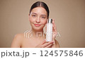 Smiling woman holds bottle with cosmetic milk. Video of attractive woman with perfect makeup on beige background. Beauty concept. Slow motion 124575846