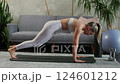 Young caucasian woman doing abdominal exercises, cardio on mat in cozy room. Gray sofa and house 124601212