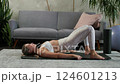 Young beautiful woman in white sportswear doing abdominal exercises, lifting hips, lying on a rug 124601213
