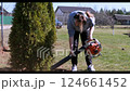 Woman using a leaf blower to clean up in a residential garden during a sunny day 124661452