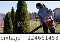 Woman using a leaf blower to tidy up shrubs in a sunny garden setting 124661453