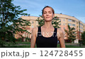 Fit woman running with focused determination along urban park pathway, residential backdrop framing athletic performance during morning exercise routine 124728455