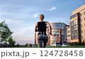 Sporty female performing dynamic stretching and running alongside contemporary apartment complex, representing vibrant city fitness lifestyle during golden hour exercise routine 124728458