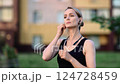 Confident blonde athlete in black sportswear fitting wireless earphones, getting ready for evening run along quiet residential street 124728459