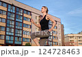 Female athlete sprinting through urban neighborhood, black tank top and gray leggings highlighting athletic physique and dynamic fitness routine 124728463