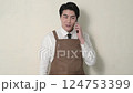 A Japanese man wearing an apron making a phone call 124753399