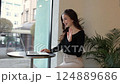Smiling young woman freelancer uses laptop in cafe for video call, waves hand hello, shows thumb up and her new braces on teeth. Modern technology, youth lifestyle, gen z. Remote communications 124889686