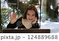 Young woman freelancer uses laptop in cafe. Video call and waves hand hello, chats in internet, smiles. Modern technology, youth lifestyle, gen z. Remote studying, e-learning, online remote work. 124889688
