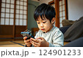 asian boy looking at phone screen, japanese child with smartphone sitting on sofa, social media addiction, chinese kid playing on phone, technology, online shopping, internet 124901233