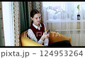 Young girl sitting in chair using smartphone indoors in cozy setting 124953264