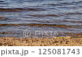 Waves calmly splash on shore. River on summer day. Sandy shore close-up. 125081743