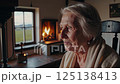 Serene Elderly Woman Enjoying Cozy Fireplace - Reflective Moment - 4k Video She gazes thoughtfully off-camera, bathed in the warm 125138413