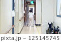 the back of an old man who uses a walking aid to walk through a hospital hallway 125145745