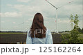 Young woman observing rotating wind turbines in a field 125162264