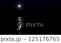 Bright full moon casts a glowing path of light across calm ocean waters at night, creating a tranquil and mysterious coastal scene 125176765