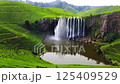 A breathtaking aerial view of a waterfall cascading down a rocky cliff into a tranquil lake, surrounded by lush green tea plantations 125409529