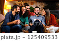 A diverse group of male and female friends sitting together in a cozy home setting, enjoying tea and warm conversation 125409533