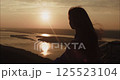 Woman watching sunset over river from mountain top 125523104