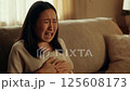A young adult Asian woman sitting on a sofa in her living room, clearly suffering from abdominal pain 125608173