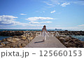 Attractive girl in white dress walking on seaside pier or breakwater 125660153