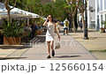 Girl in white dress walks in Ibiza old town street, look at camera, spinning 125660154