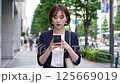 一位女士走在城市裡，看著她的智慧型手機 125669019