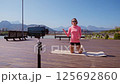 Female fitness instructor records a workout video on a smartphone camera in a public park. She is 125692860