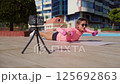 Young woman follows an online workout in a public park on a sunny day. She watches exercise 125692863