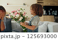 Young boy gives his mother a bouquet of flowers at home in a warm and cozy setting. She smiles with 125693000