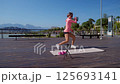 Young athletic woman in bright pink sportswear follows an online workout on a yoga mat in a public 125693141