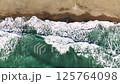 Aerial view capturing emerald green waves breaking over golden sand, white foam cascading along pristine coastal landscape with serene marine scenery 125764098