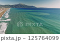 Turquoise waves breaking against golden sand, revealing mountain silhouettes under bright sunlight, mediterranean waters reflecting serene coastal scenery 125764099