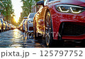 Luxury red sports car with led headlights parked on wet cobblestone street at sunset, front view detail showing reflection and premium design elements among vehicles 125797752