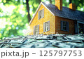 Yellow house model sitting on pile of dollar bills with green bokeh background, representing real estate investment, property value, mortgage financing and home ownership concept 125797753